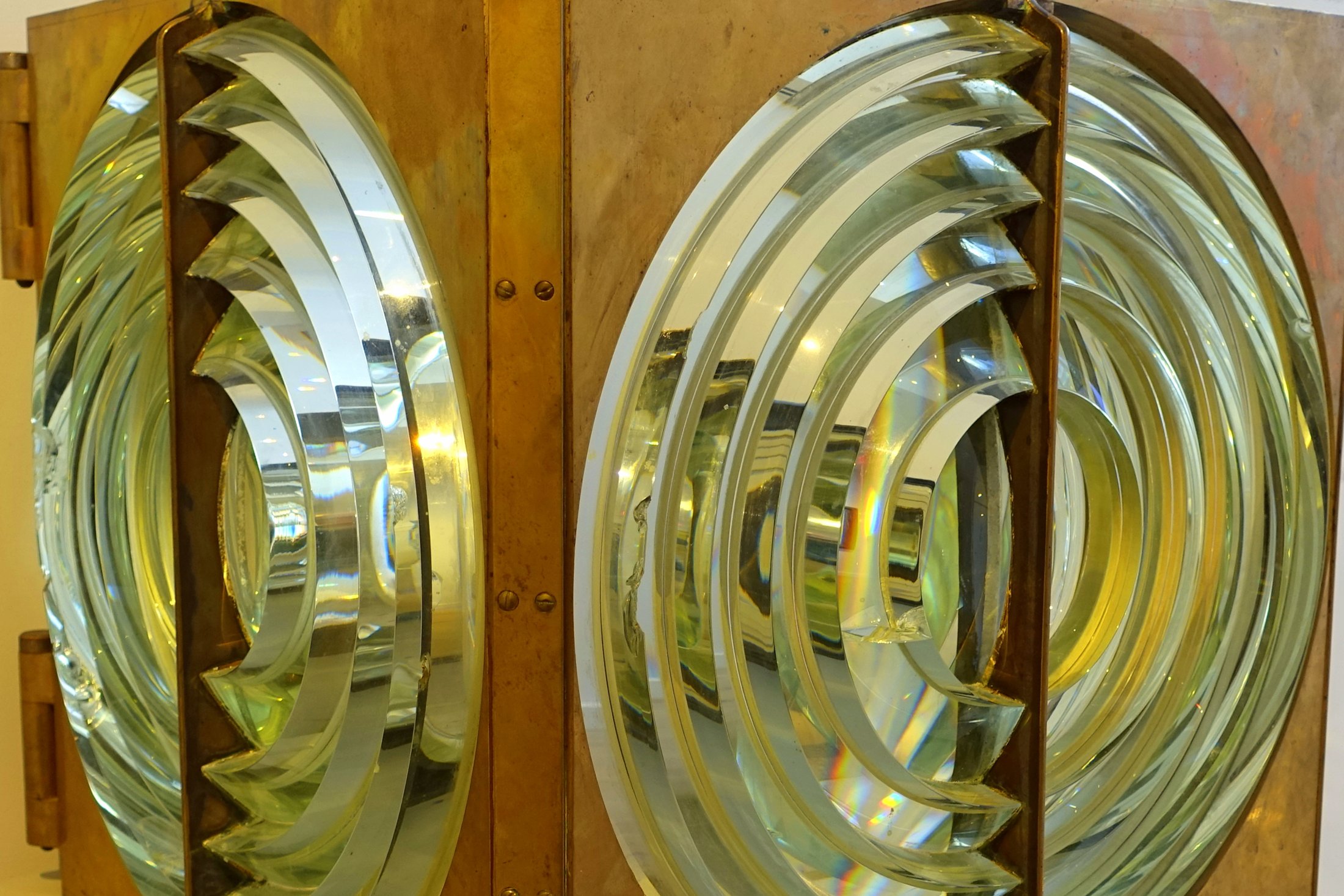 Close-up of a nineteenth-century Fresnel lighthouse lens: two brass-framed panels of concentric glass rings, each a bullseye that gathers light into a beam.