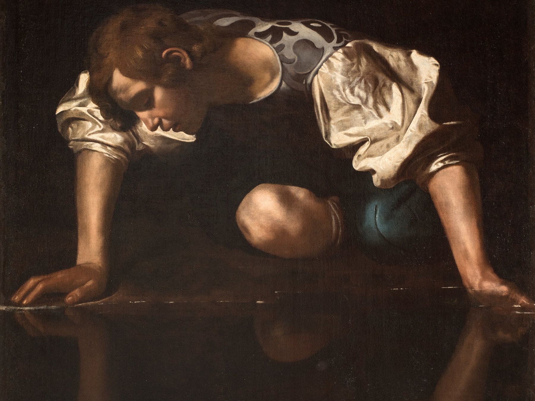 Painting of Narcissus attributed to Caravaggio: a young man in a white shirt and brocade vest leans over dark water on his hands and one knee, gazing down at his own reflection.